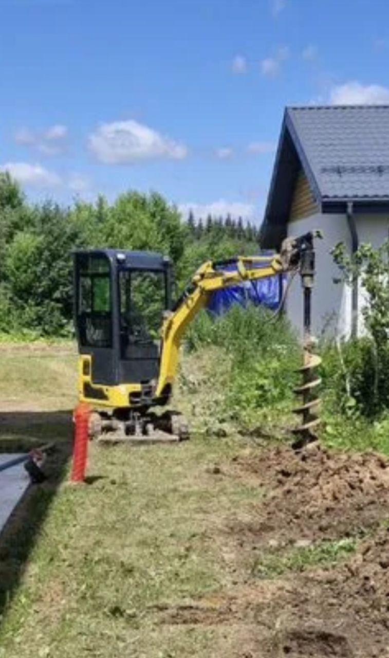 Жёлтый мини-экскаватор Rippa с большим гидробуром на стреле, шнек около 300 мм опущен в землю на участке